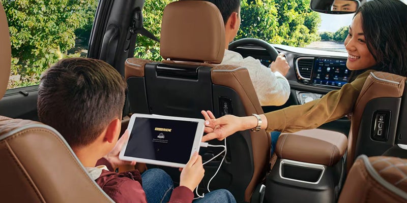 Interior view of a minivan with passengers in the front and rear seats, showing a child using a tablet connected