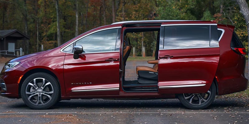 Side view of a red minivan with the power sliding door open, revealing the spacious passenger cabin and second-row seating