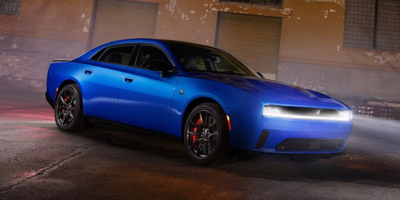 Blue two-door muscle car parked on a wet street at night, with bright LED headlights illuminated