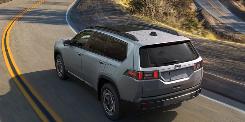Silver SUV viewed from the rear driving along a winding two-lane road through a hilly landscape