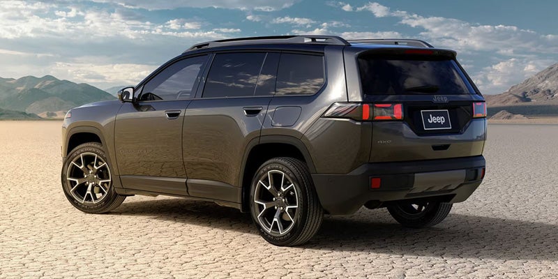 Dark gray SUV parked on a dry lakebed with mountains and a cloudy sky in the distance