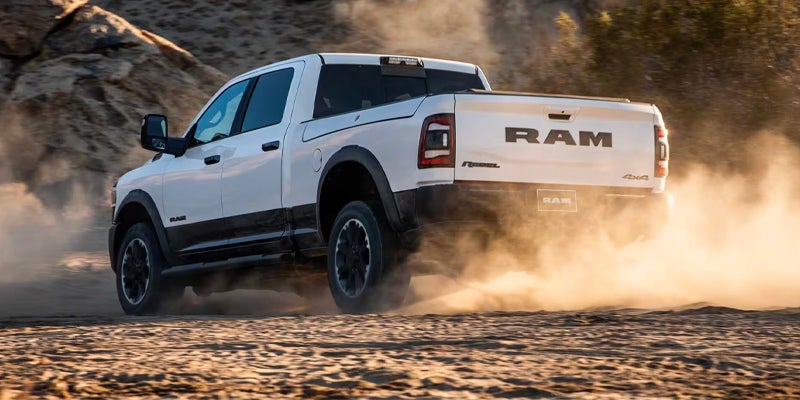 White Ram Rebel pickup truck kicking up dust on a dirt road, seen from the rear passenger side