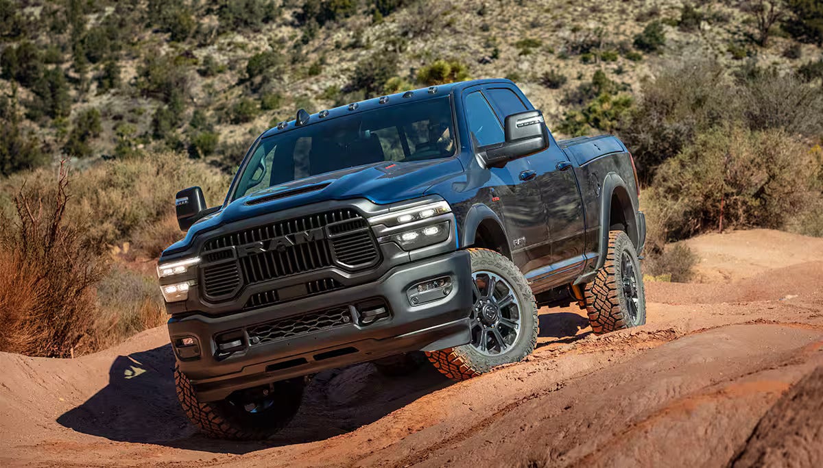 Dark blue Ram Power Wagon truck driving on a dusty, rocky off-road trail in a desert landscape