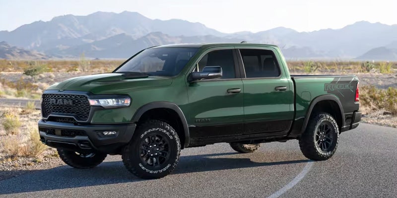 Dark green full-size pickup truck parked on a paved road in a desert landscape, with mountains visible in the background under daylight