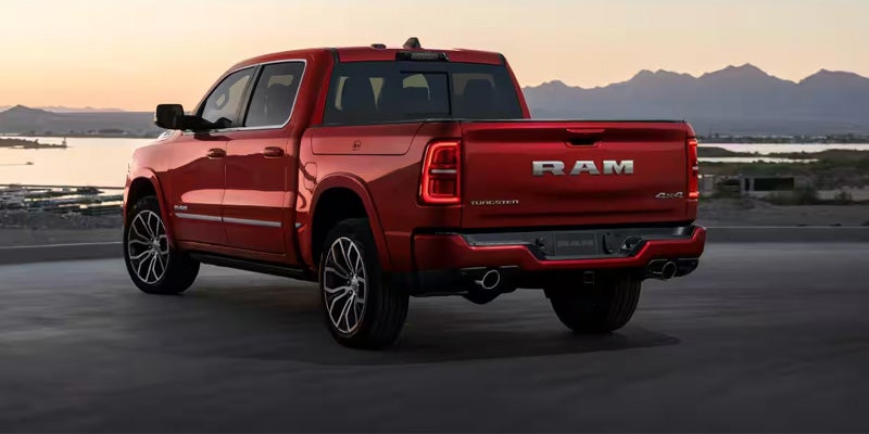 Rear three-quarter view of a red pickup truck parked near a waterfront at sunset, with mountains visible in the distance