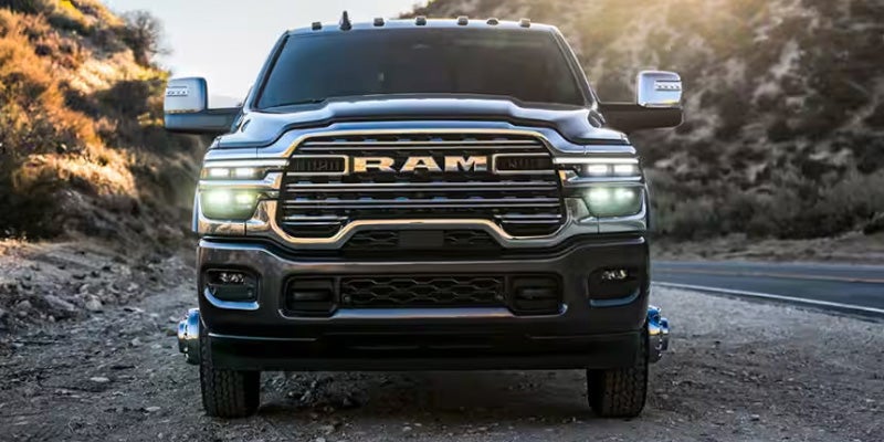 Front view of a black heavy-duty pickup truck with illuminated headlights on a mountain road